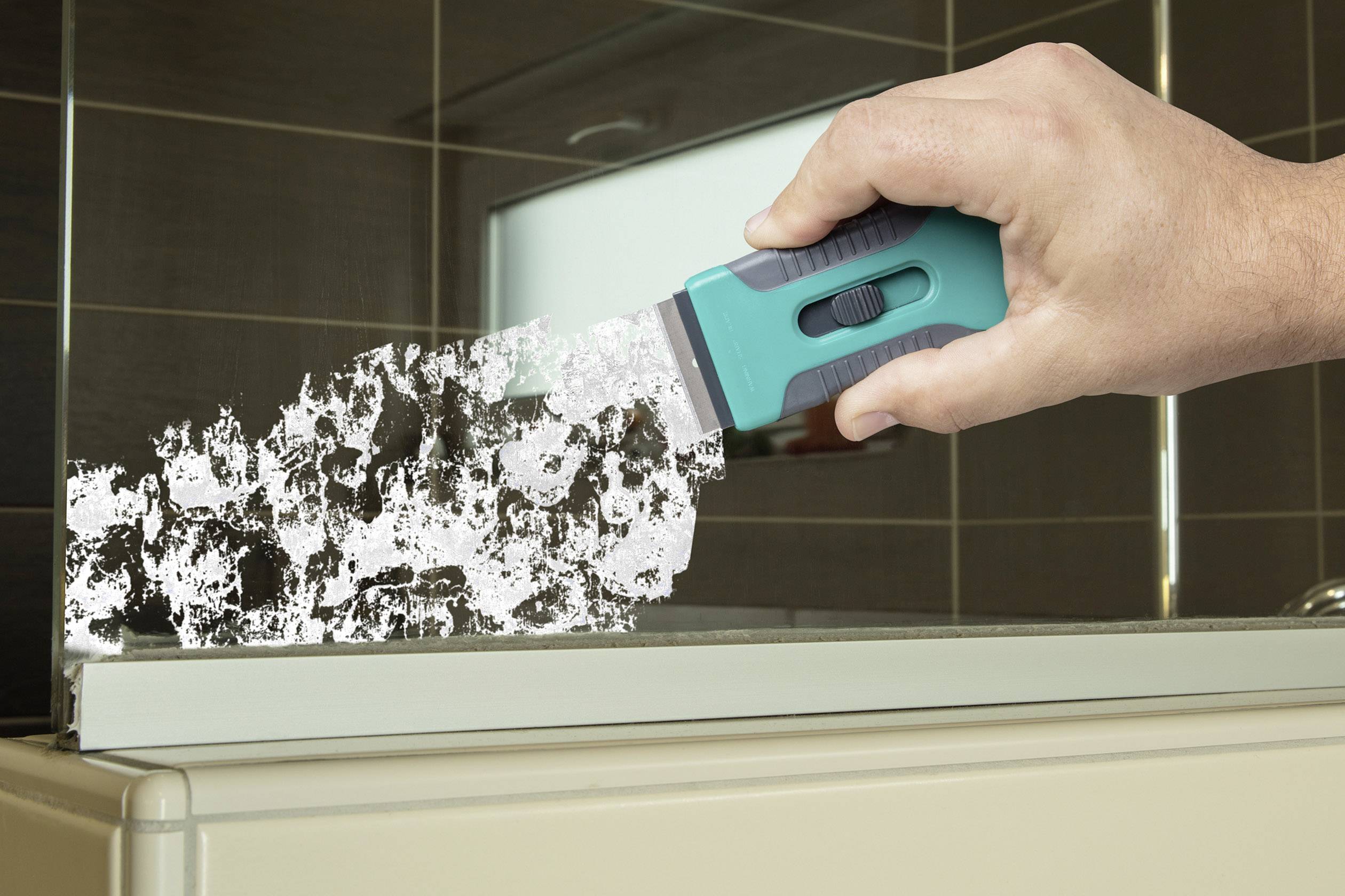 Eine Hand hält einen grünen Schaber und entfernt hartnäckigen Schmutz von einer Glasoberfläche in einem Badezimmer.