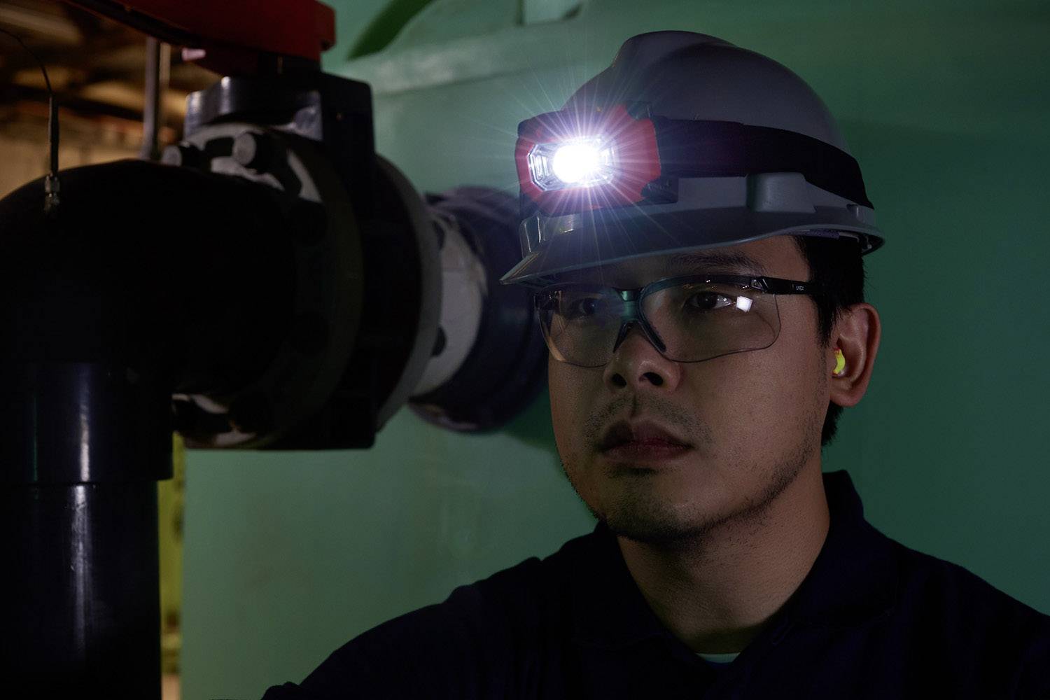 Ein Mann trägt einen Helm mit Stirnlampe und Schutzbrille, arbeitet in einer industriellen Umgebung.