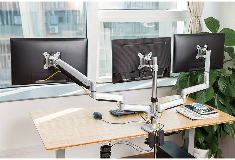Zwei Monitore auf einem höhenverstellbaren Schreibtischarm in einem Büro, mit Tastatur, Maus und Notizbüchern daneben.