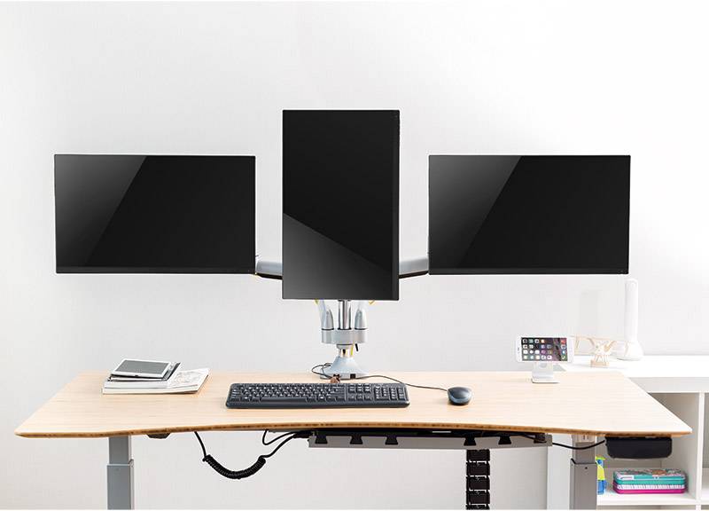 Drei Computermonitore auf einem höhenverstellbaren Schreibtisch. Der mittlere Monitor ist vertikal ausgerichtet. Darunter eine Tastatur.