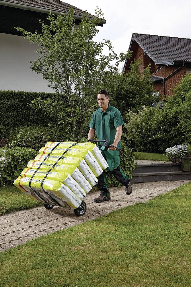 Ein Mann in grüner Arbeitskleidung schiebt einen Handwagen voller gelber Säcke auf einem gepflasterten Weg vor einem Wohnhaus.