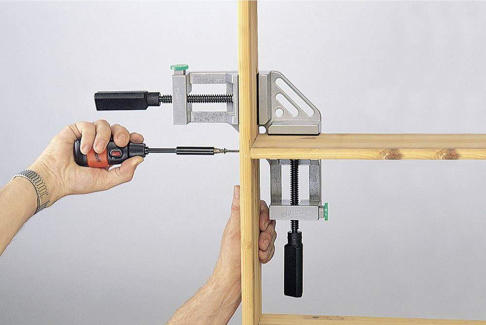 Eine Person befestigt ein Holzregal mit zwei Schraubzwingen und einem Schraubendreher.