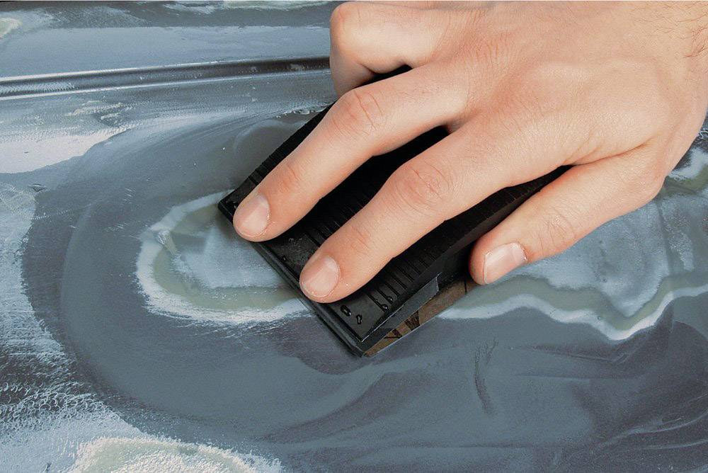 Hand schleift mit einem Schleifklotz Metalloberfläche. Fokus auf Handbewegung und Textur des geschliffenen Metalls.