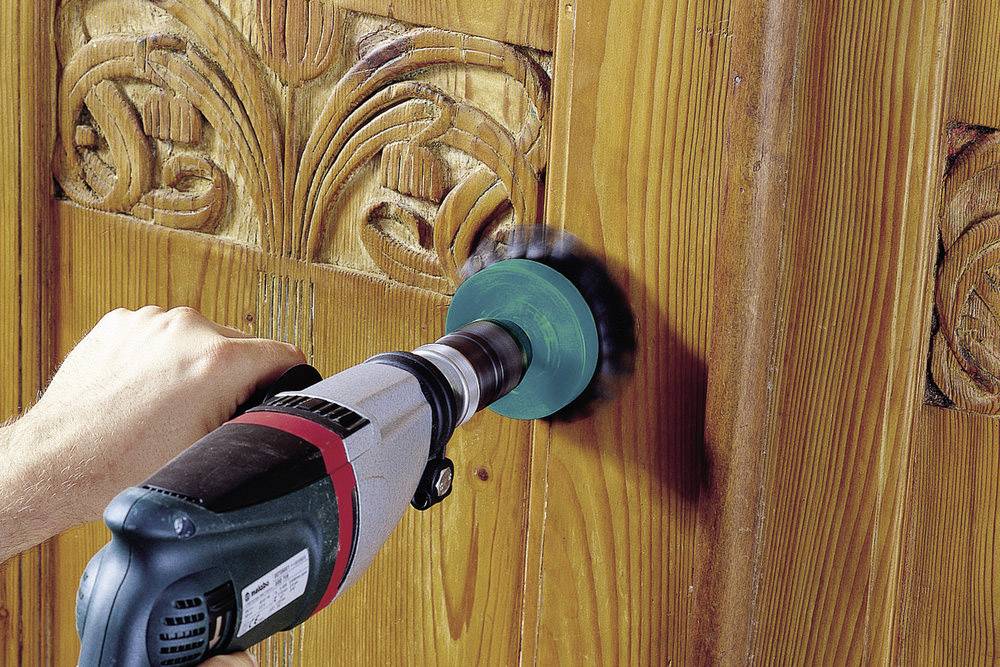 Eine Person verwendet eine Schleifmaschine auf einer Holzoberfläche mit dekorativen Schnitzereien.