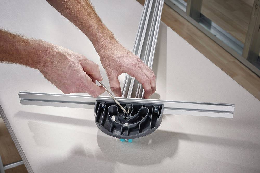 Eine Person montiert ein Metallgestell mit einem Schraubendreher. Das Gestell liegt auf einem Tisch in einem Innenraum.