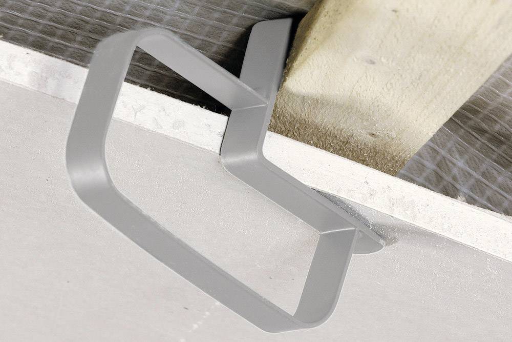 Metallaufhängung befestigt eine rechteckige Gipsplatte an einem Holzbalken. Die Konstruktion ist Teil einer Deckeninstallation.