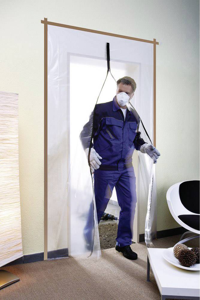 Ein Mann in Schutzkleidung und Maske tritt durch eine transparente Plastik-Absperrung in einen Raum ein.