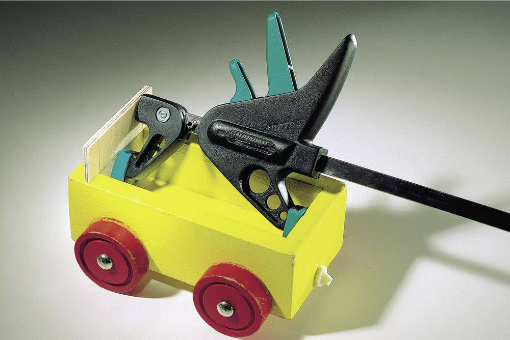 Gelbes Spielzeugauto mit roten Rädern, das eine schwarze Zwinge transportiert. Das Auto steht auf einer hellen Oberfläche.