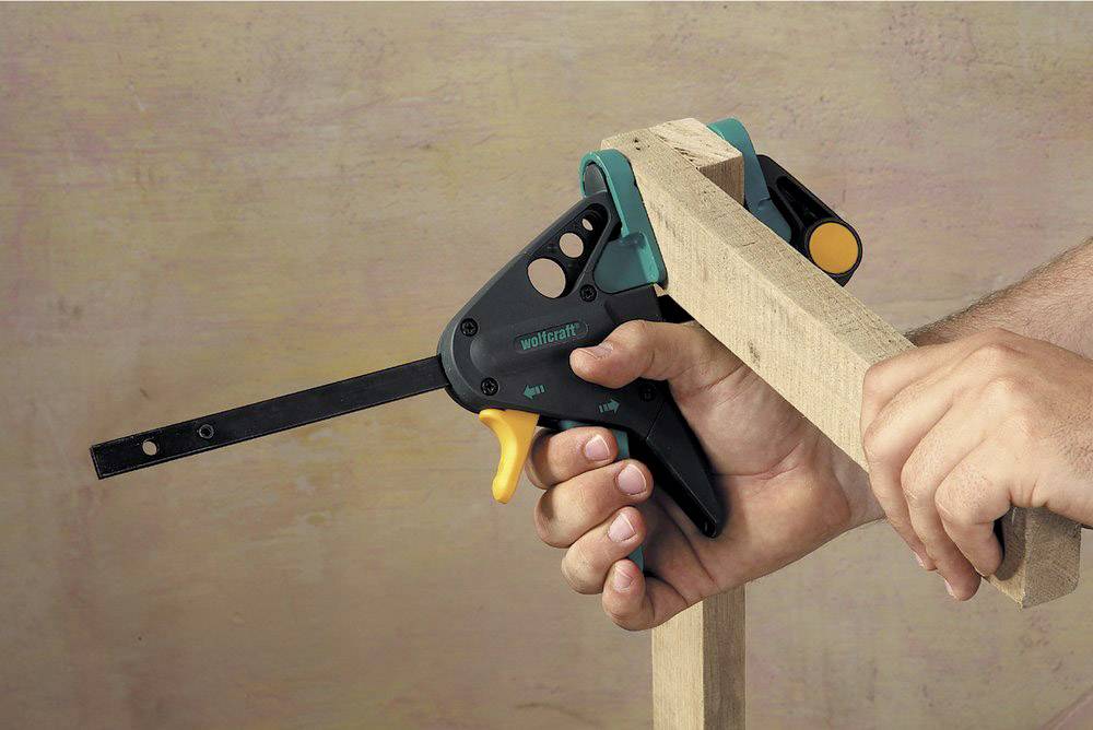 Eine Hand hält eine Klemme, die ein Holzstück fixiert, um es zusammenzubauen.