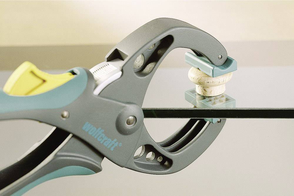 Eine Zwinge hält ein Glasstück mit einem kleinen, runden Dämpfer an der Kante. Geeignet für den sicheren Transport oder die Bearbeitung von Glas.