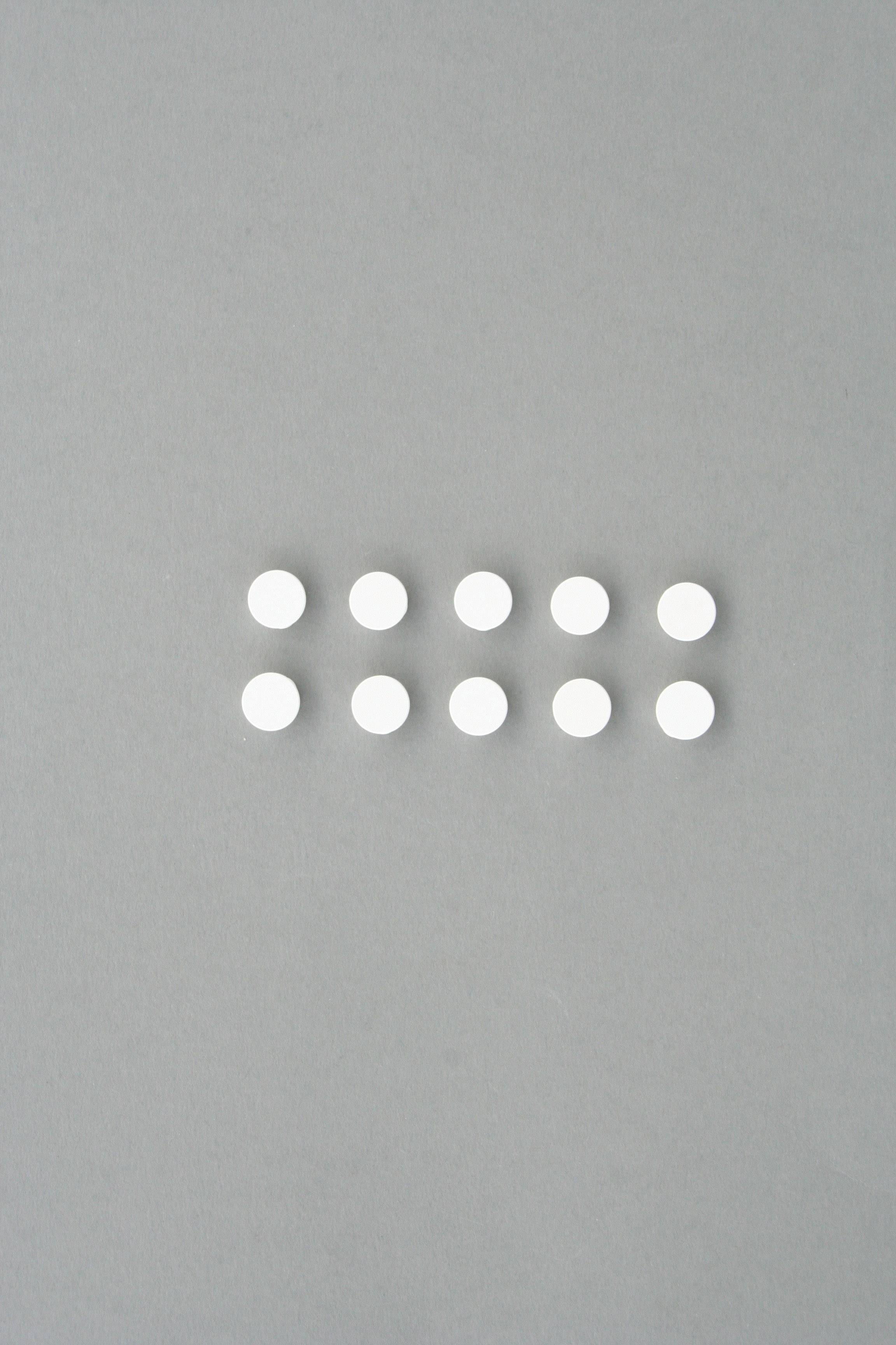 Zehn weiße, runde Tabletten auf grauem Hintergrund, in zwei Reihen zu je fünf Tabletten angeordnet.