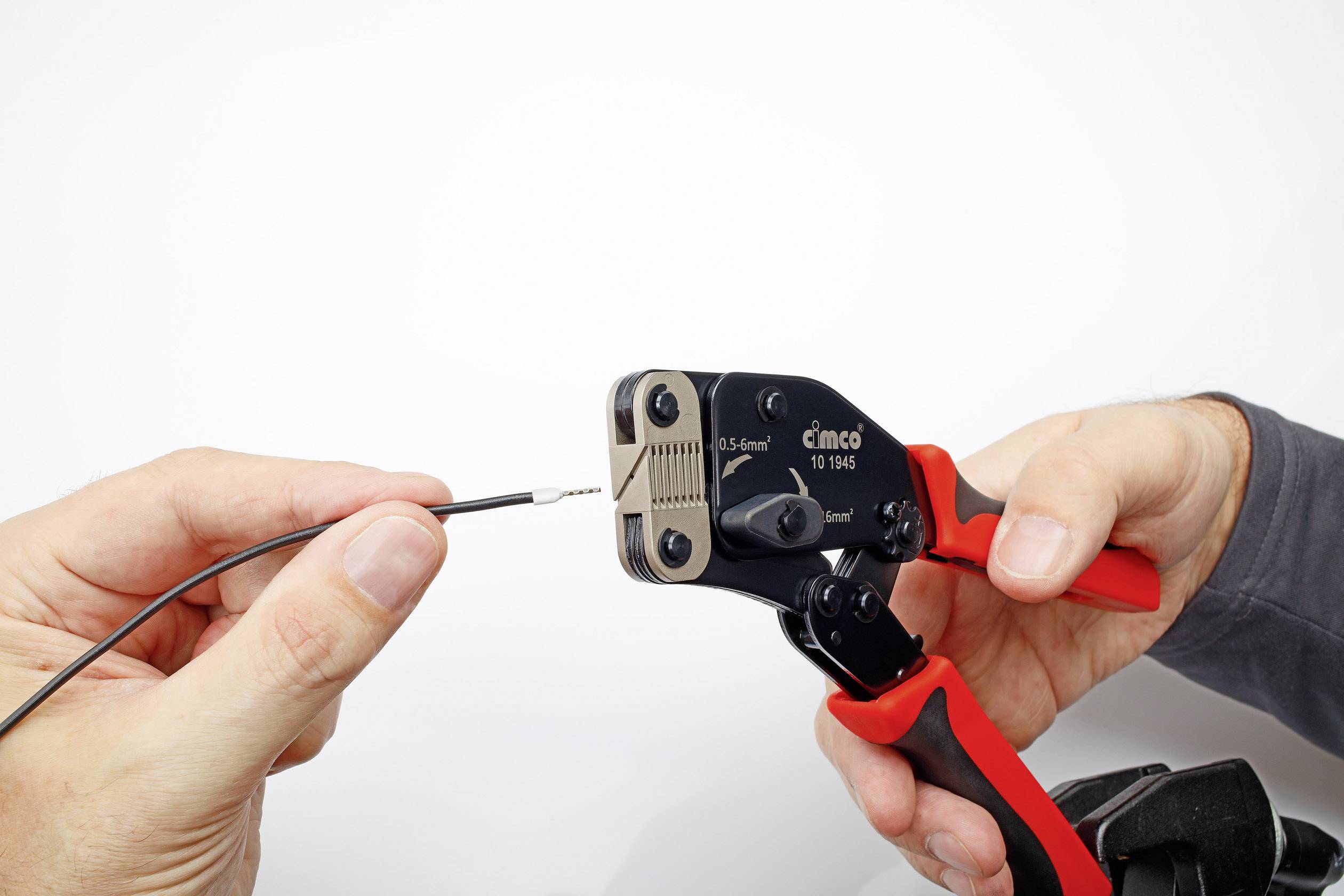 Zwei Hände halten ein Kabel und eine Crimpzange. Die Zange wird verwendet, um ein Verbindungselement auf das Kabelende zu crimpen.