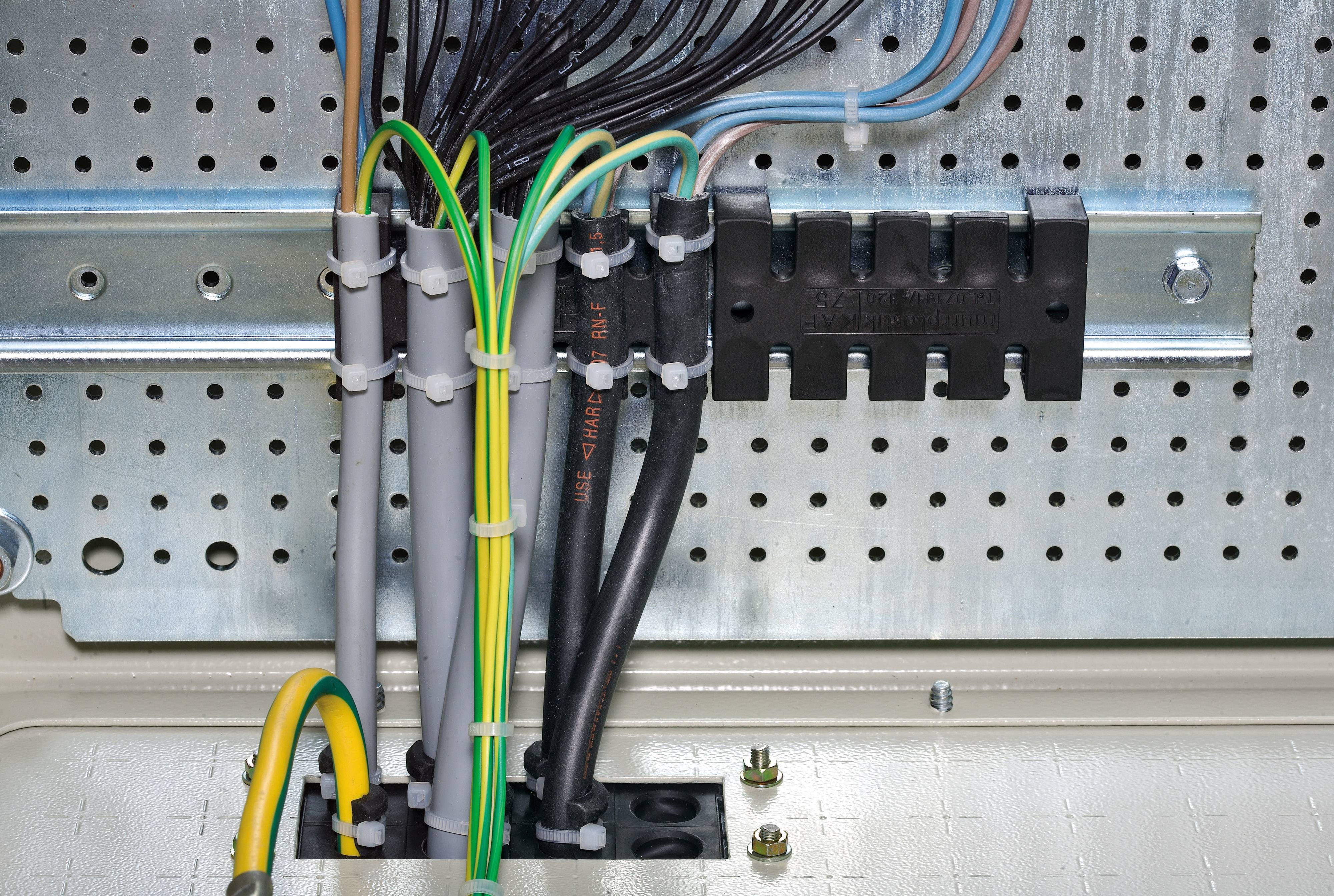 Verkabeltes elektrisches Anschlusspanel mit mehreren schwarzen und grauen Kabeln, erdet mit gelb-grünem Kabel, vor metallischer Rückwand.