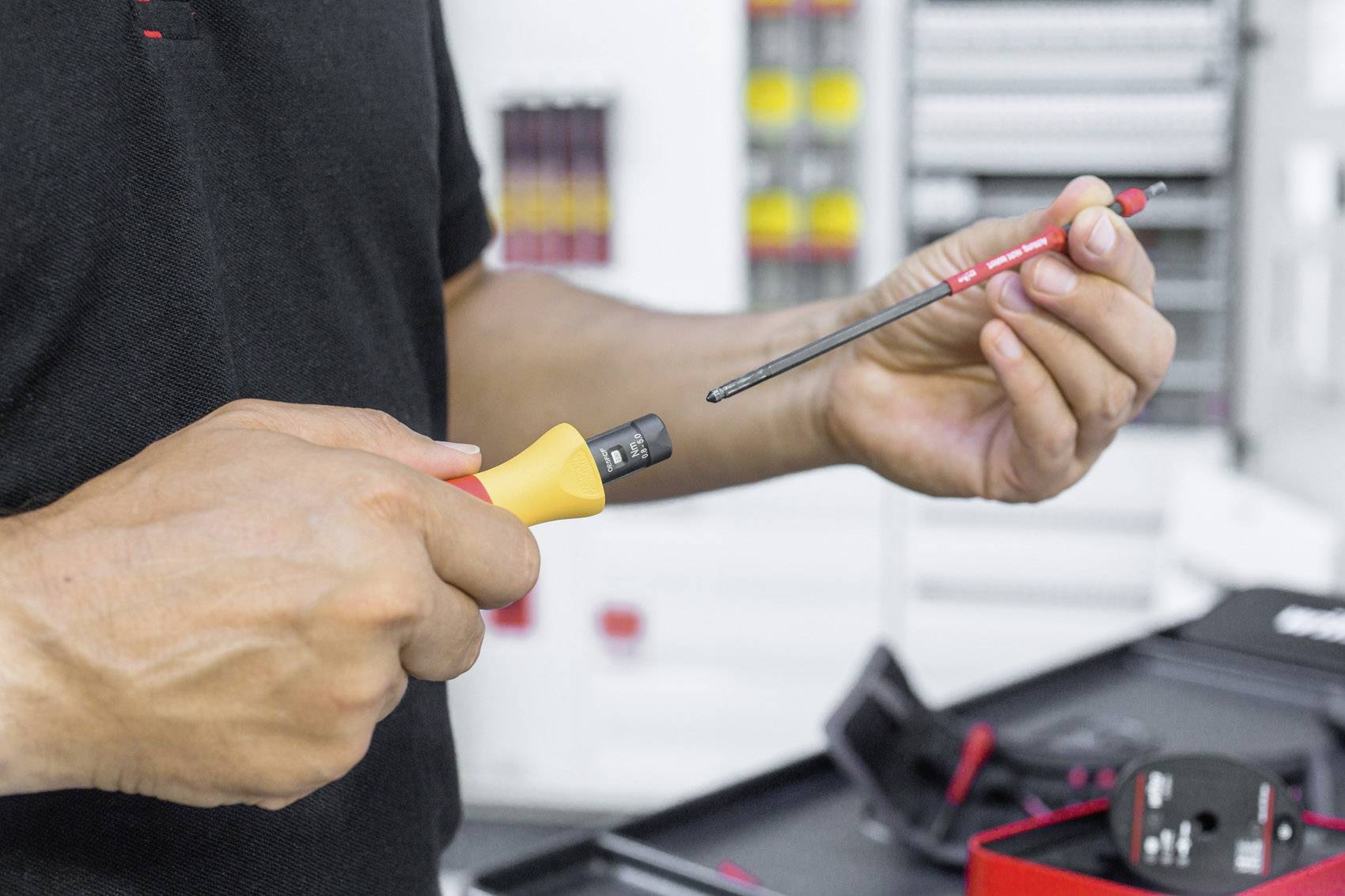 Eine Person hält einen Schraubendreher und eine eingeschaltete elektrische Prüfvorrichtung in einer Werkstatt.