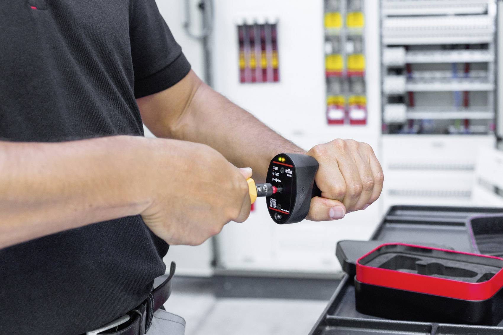 Eine Person testet mit einem elektrischen Messgerät in einem technischen Raum mit Schaltkästen im Hintergrund.