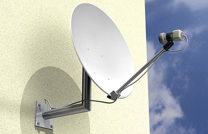 Satellitenschüssel an einer Wand montiert, zeigt nach oben gegen einen blauen Himmel mit wenigen Wolken.