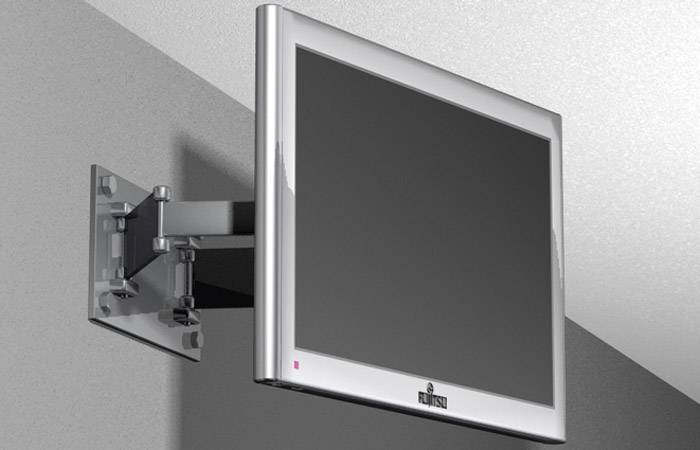 Flatscreen-Monitor an einer verstellbaren Wandhalterung, montiert in einem Raum mit grauen Wänden.