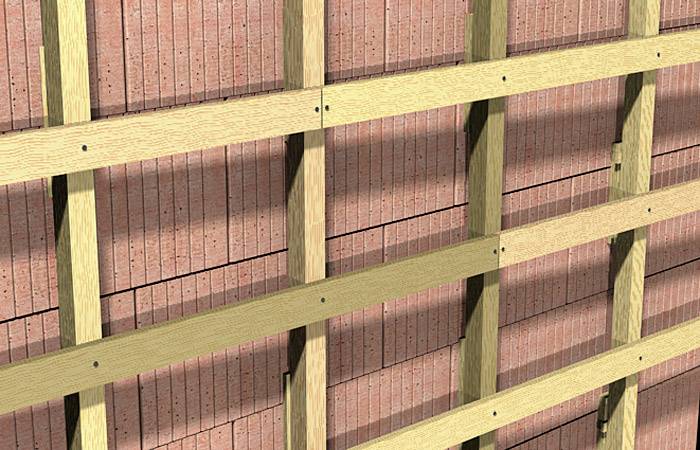 Das Bild zeigt eine Holzlattenkonstruktion auf einer Ziegelmauer. Die Latten sind in regelmäßigen Abständen horizontal und vertikal angebracht.