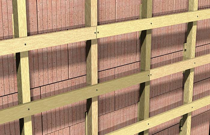 Holzlattenkonstruktion vor einer Ziegelwand; dient als Unterkonstruktion für Fassadenverkleidungen zur Wärmeisolierung.