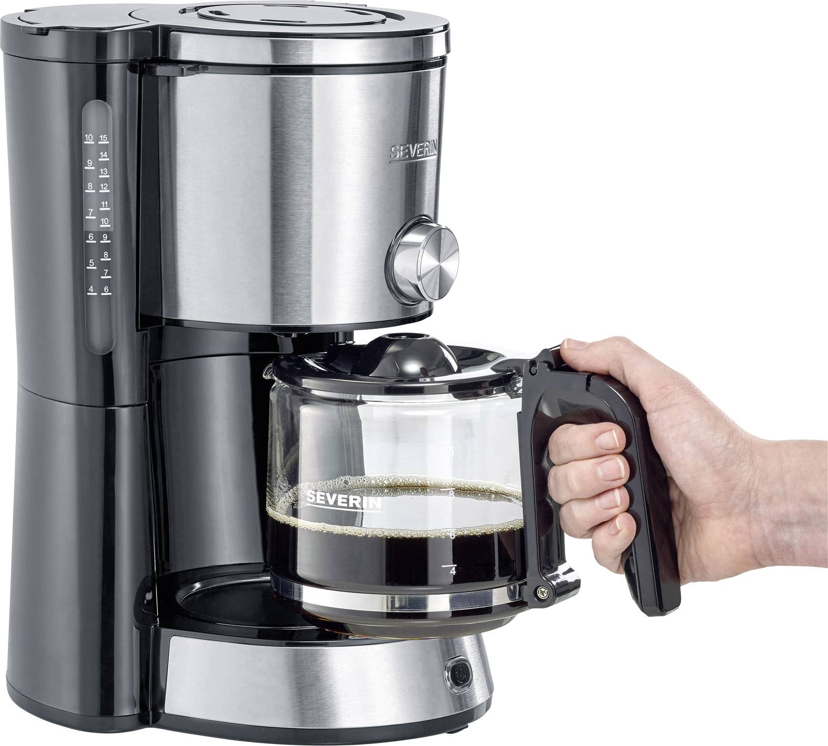 Eine Hand hält eine Glaskanne mit frisch gebrühtem Kaffee, der aus einer silbernen Kaffeemaschine fließt.