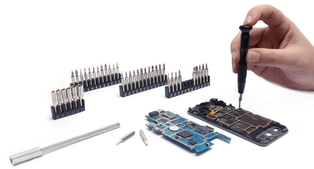 Hand hält Schraubendreher und arbeitet an Smartphone-Platine, umgeben von Schraubendreherbits und Werkzeugen.
