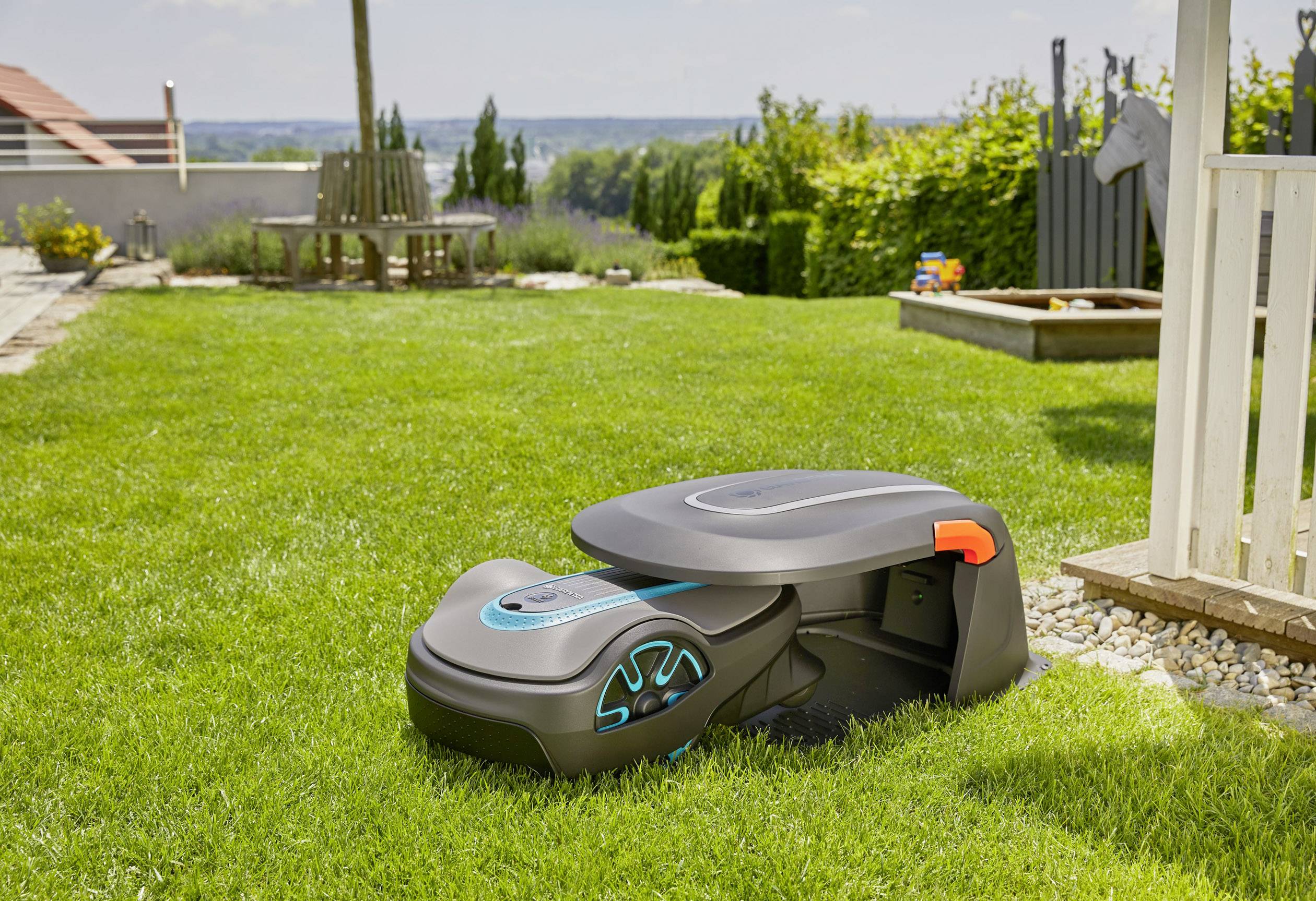 Ein Mähroboter auf einem Rasen in einem Garten. Umgeben von Bäumen und Gartenmöbeln, deutet auf eine gepflegte Umgebung hin.