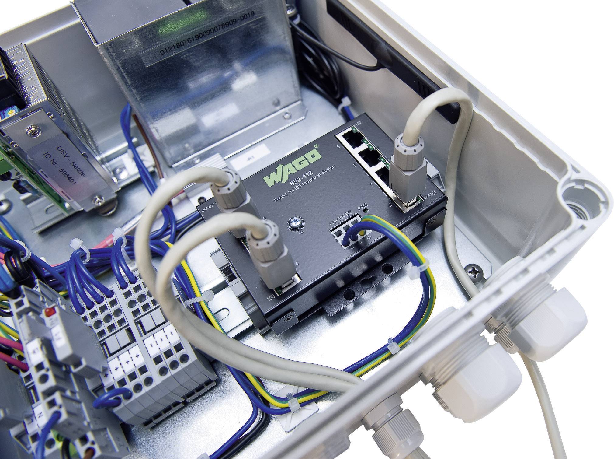Ein offenes Elektronikgehäuse mit einem Netzwerk-Switch der Marke WAGO, verbunden durch Kabel. Verschiedene Anschlüsse sichtbar.