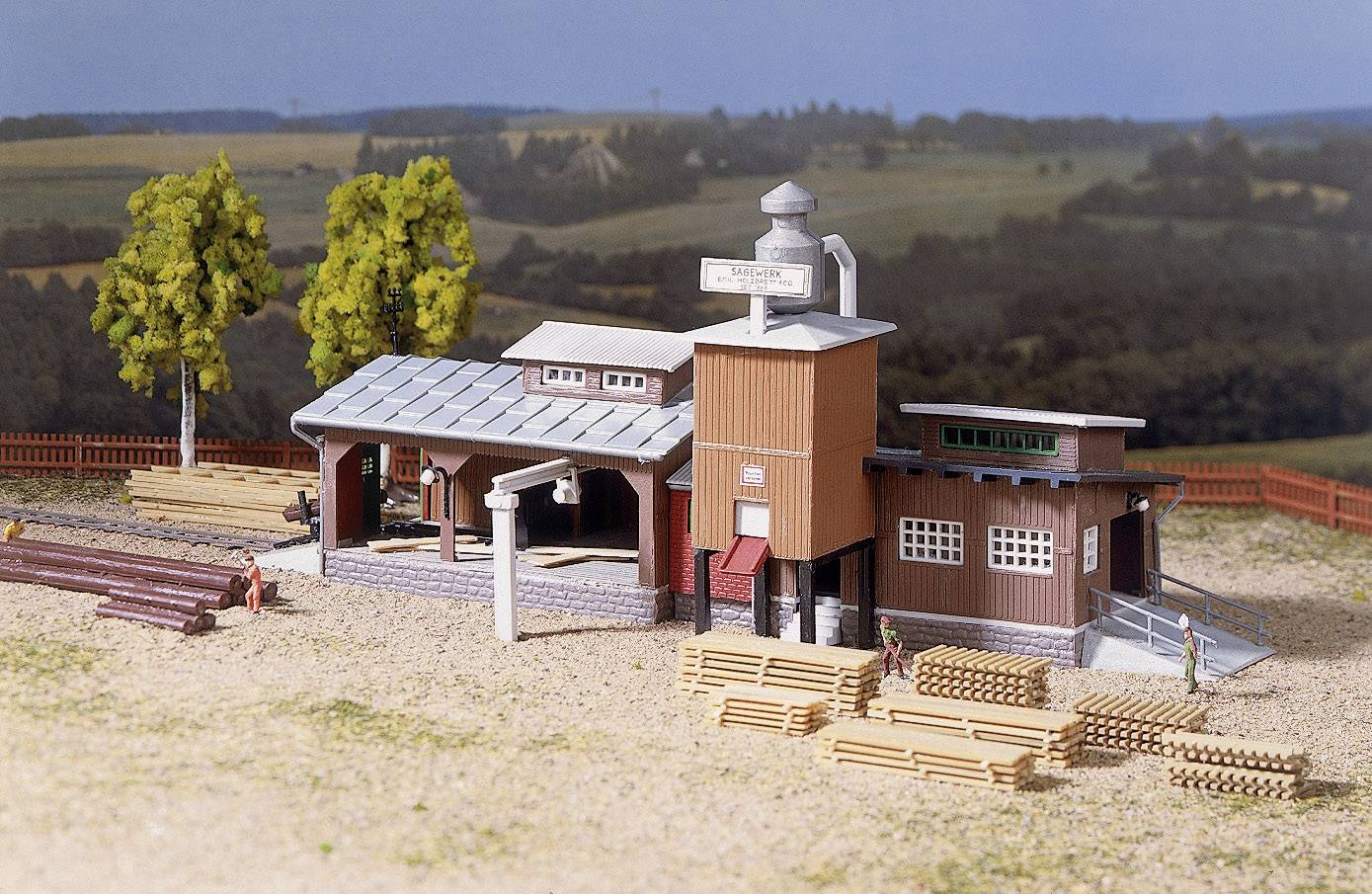 Modell einer Holzverarbeitungsfabrik mit Gebäuden, Stapeln von Holzplanken und Menschen in einer ländlichen Umgebung.
