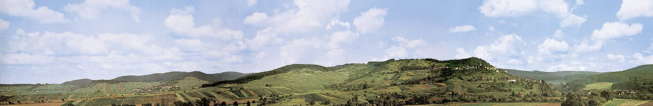 Panoramablick auf eine grüne Hügellandschaft unter blauem Himmel mit weißen Wolken.