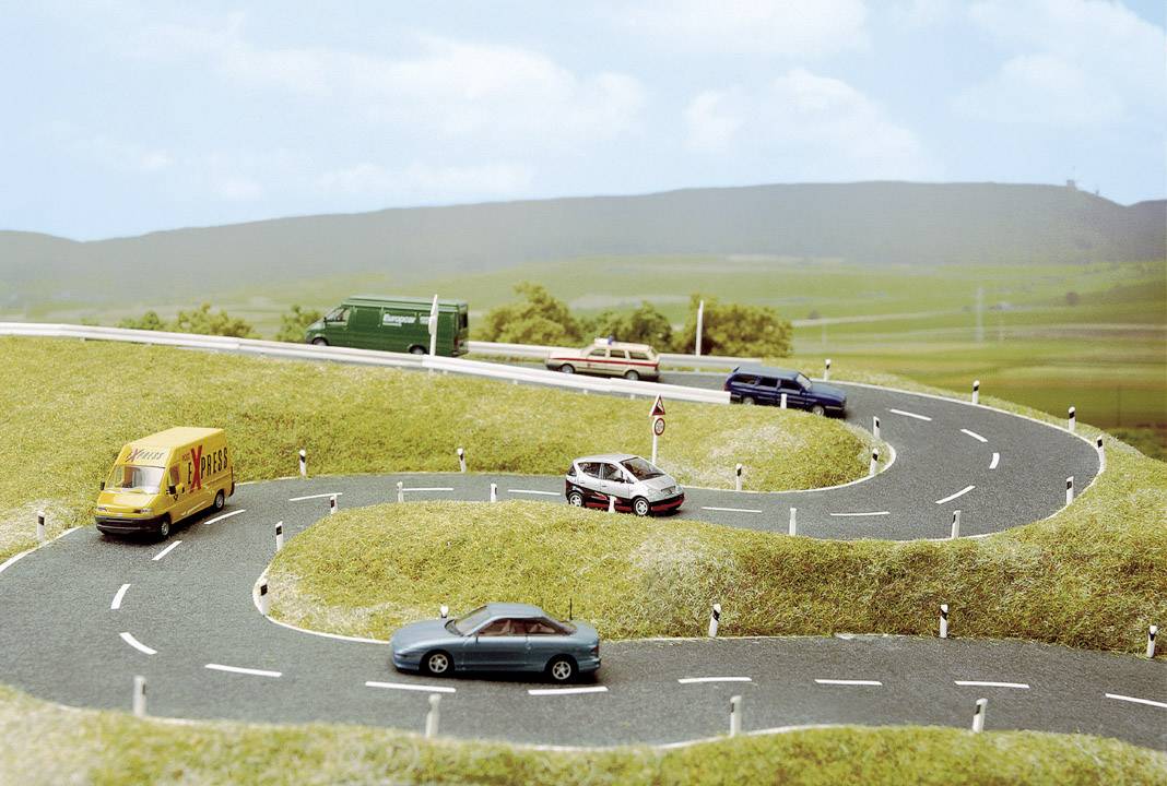 Verschlungene Straße in ländlicher Landschaft mit Modellautos, die verschiedene Fahrzeugtypen darstellen.