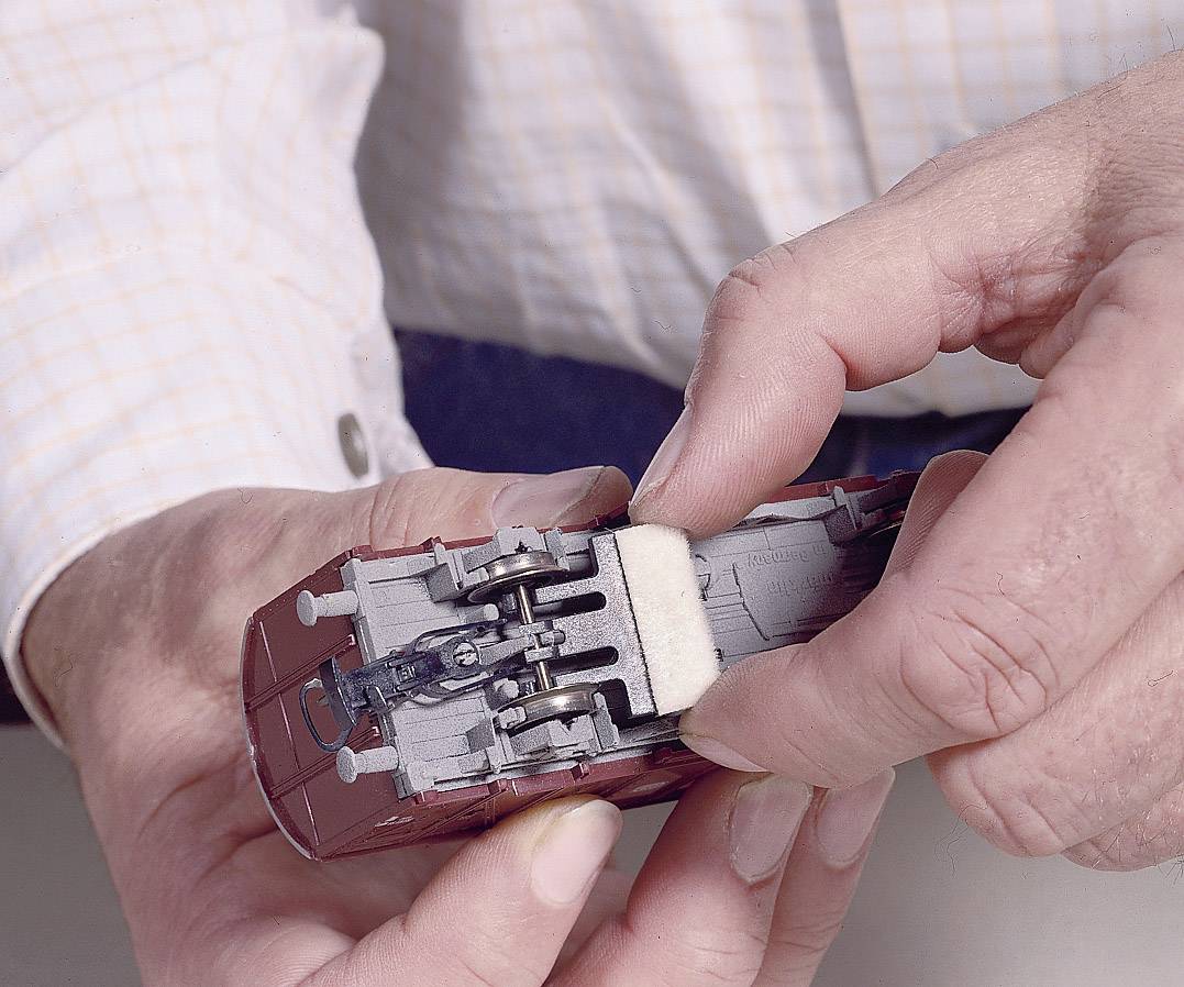 Eine Person hält ein Modellzugwagen-Prototyp und entfernt vorsichtig einen winzigen Schwamm von dessen Unterseite mit den Fingern.