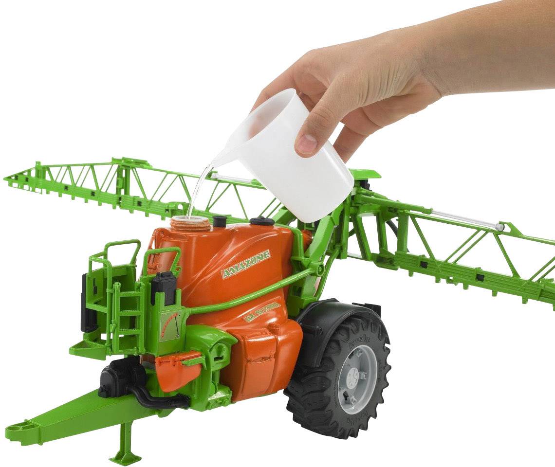 Eine Hand gießt Flüssigkeit aus einem weißen Becher in den Tank eines grünen und orangefarbenen Landwirtschaftsmodells mit Reifen und Armen.