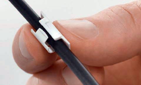 Eine Hand hält ein schwarzes Kabel mit einem kleinen, weißen Kabelclip befestigt. Der Clip organisiert und fixiert das Kabel.