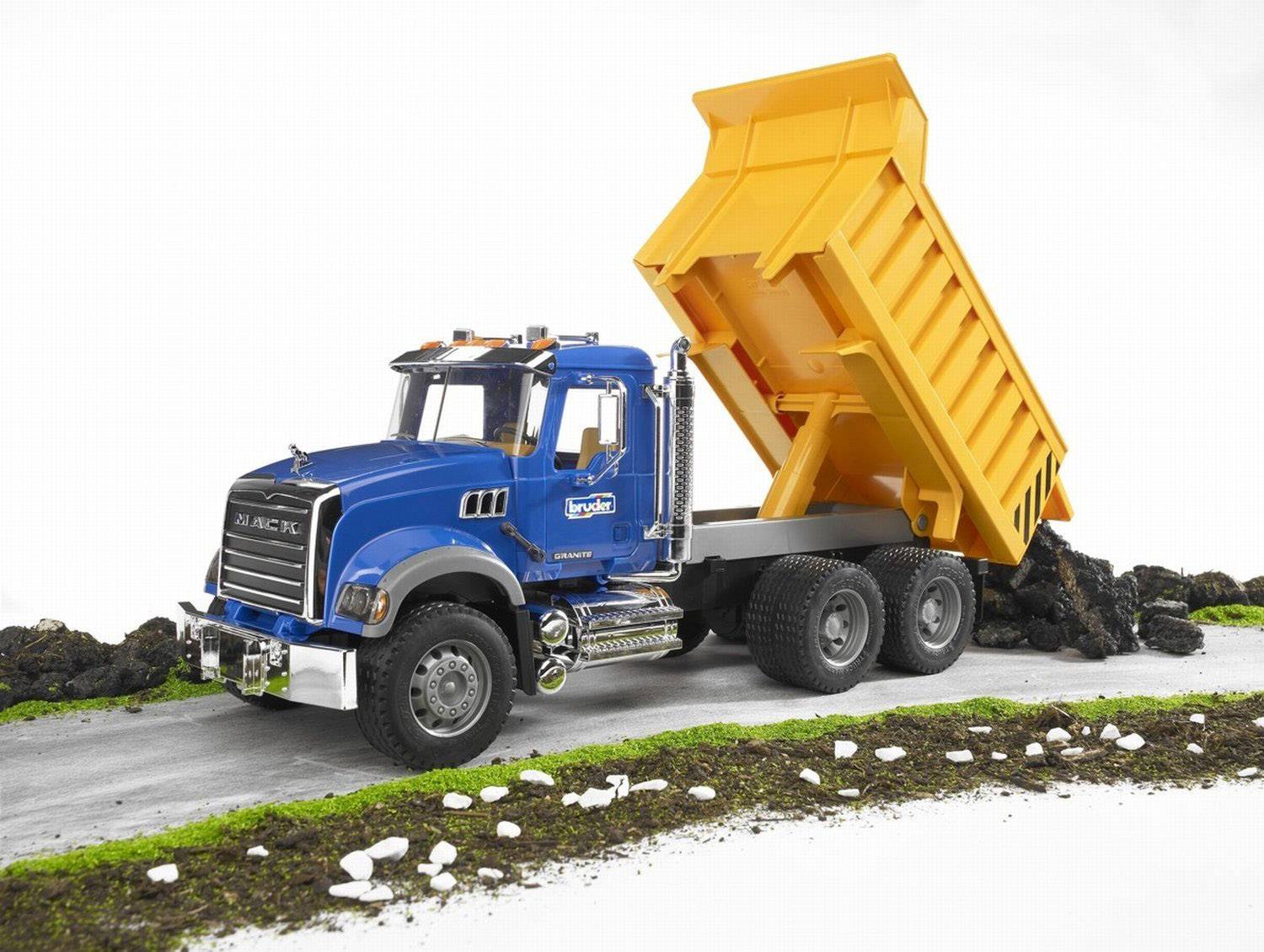 Ein blauer Spielzeug-Lkw mit gelber Kippmulde kippt Steine auf eine Straße. Der Lkw ist detailliert und steht auf grünem Untergrund.