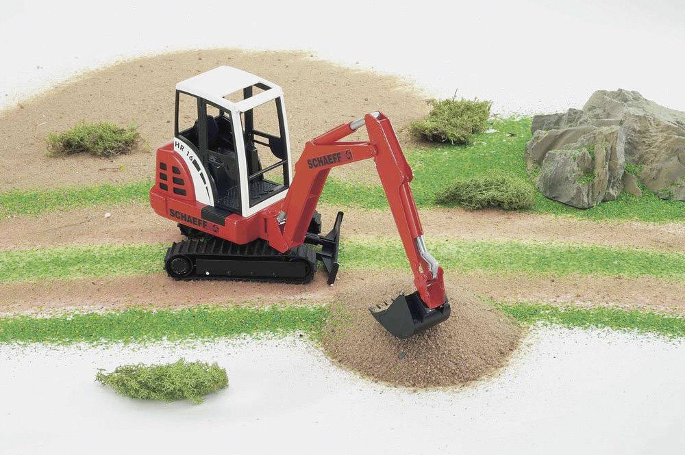 Ein roter Spielzeugbagger gräbt in einer Miniaturlandschaft mit Gras und Felsen.