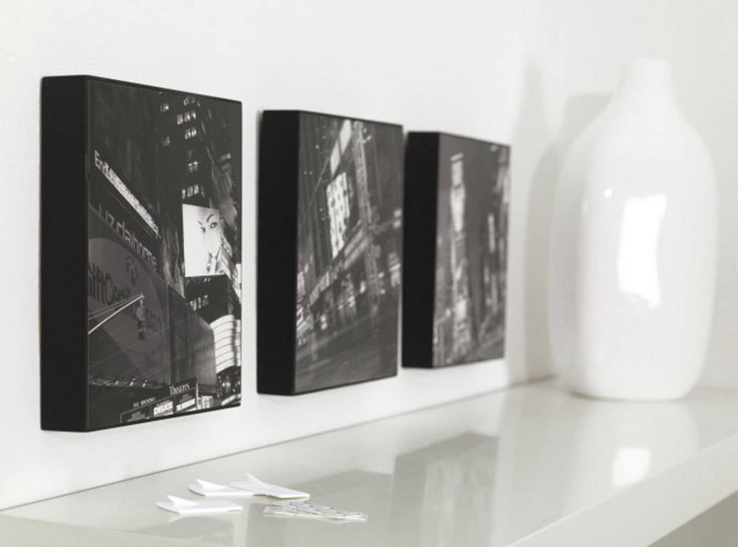 Drei Schwarz-Weiß-Fotografien von städtischen Szenen nebeneinander auf einem Regal, mit einer weißen Vase daneben.