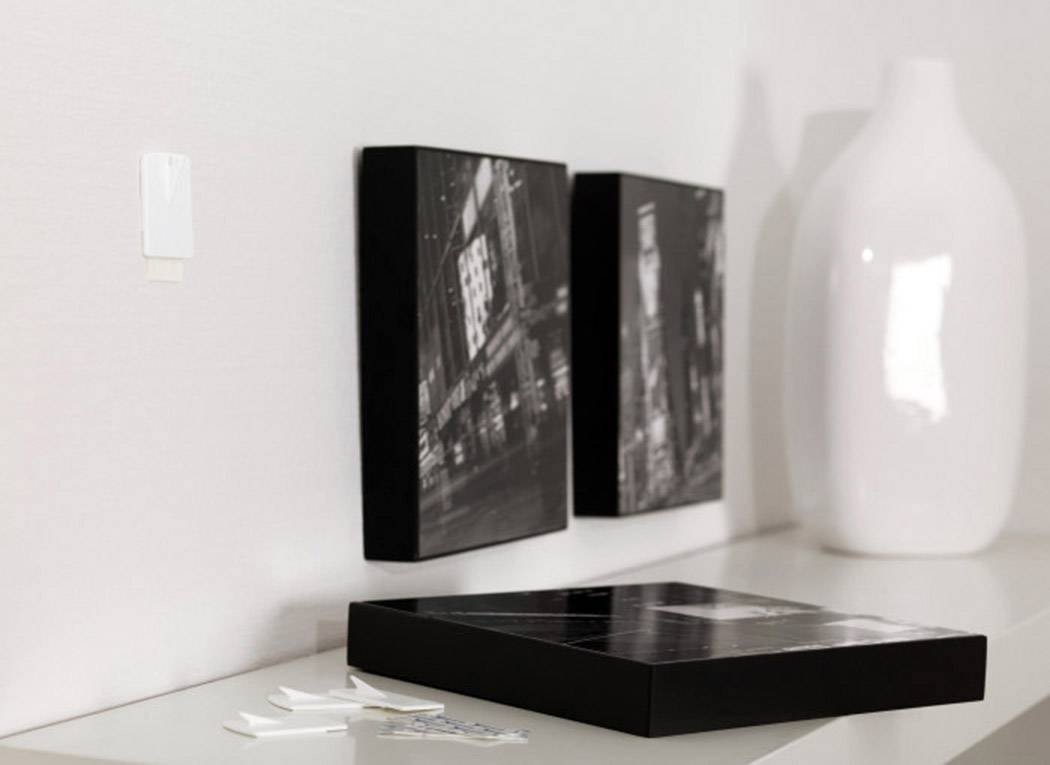 Zwei schwarz-weiße Bilder lehnen an einer Wand; daneben eine große weiße Vase. Auf dem Regal liegen Klebehaken.