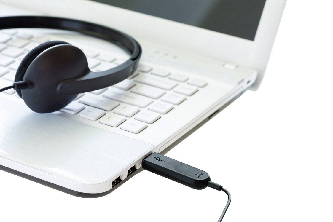 Ein schwarzes Headset liegt auf der Tastatur eines weißen Laptops, der über einen USB-Stick rechts verbunden ist.