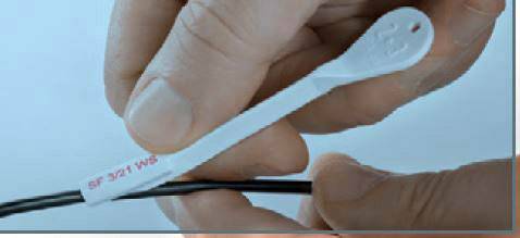 Eine Hand hält ein weißes Kunststoffband mit der Aufschrift '3M 12 NE 25°F', das um ein schwarzes Kabel gewickelt ist.