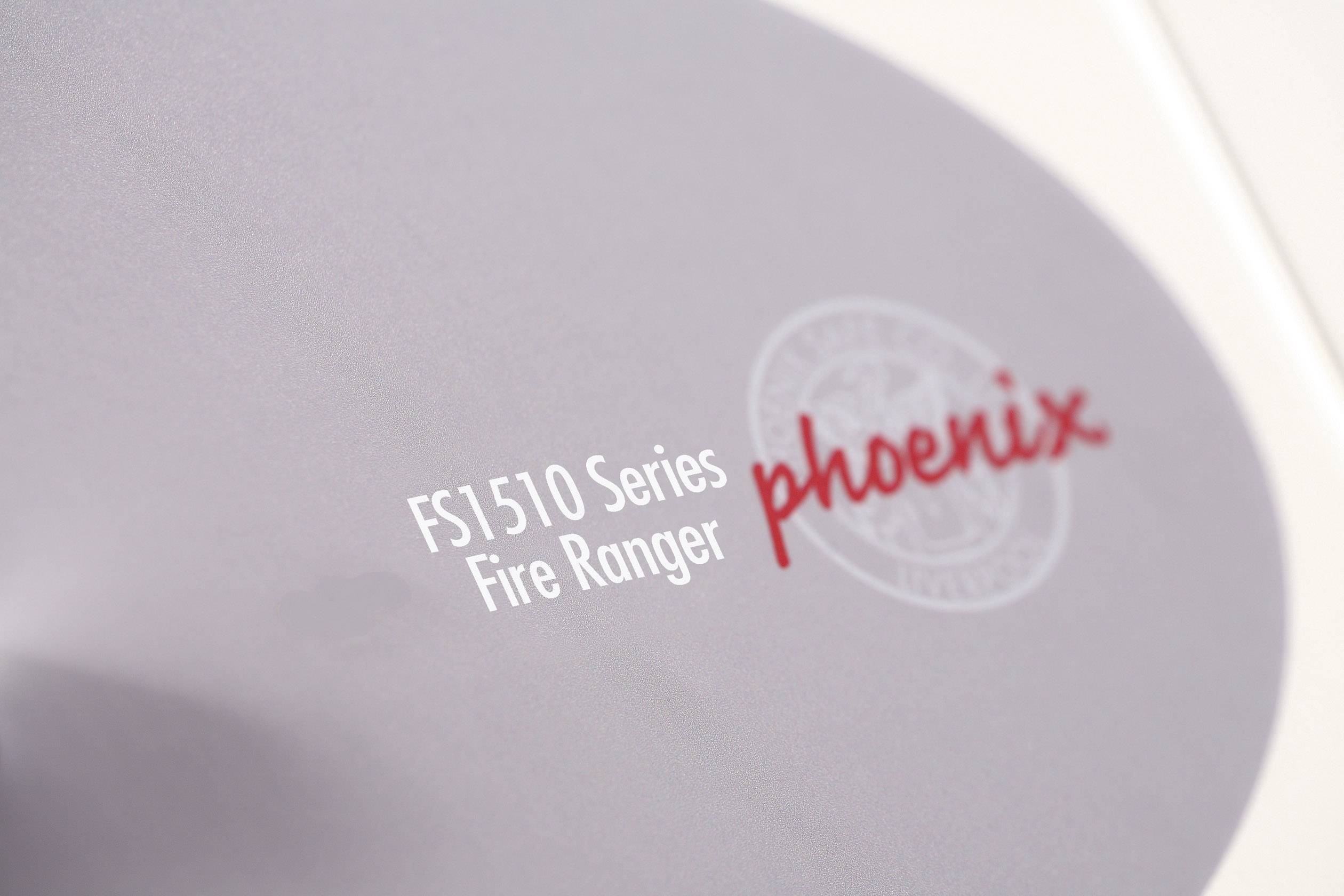 'FS1510 Series Fire Ranger phoenix' steht auf einer grauen Fläche mit einem kreisförmigen Logo, das matt und kaum erkennbar ist.