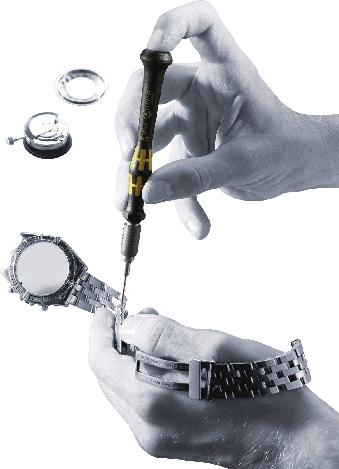 Eine Person repariert eine Armbanduhr mit einem Schraubendreher. Einzelteile der Uhr sind im Hintergrund zu sehen.