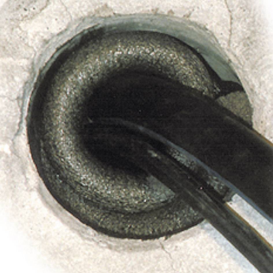 Nahaufnahme eines schwarzen Elektrokabels, das durch ein Betonloch verläuft. Das Bild fokussiert auf die Kabelabschirmung.