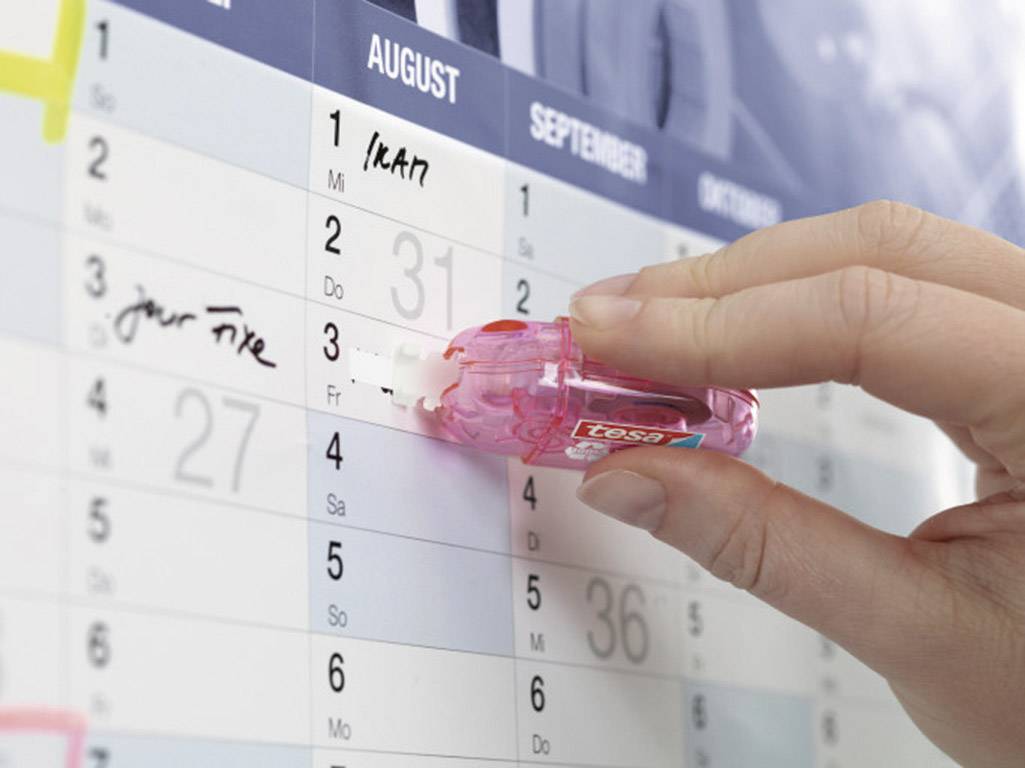 Eine Hand benutzt einen Korrekturroller auf einem Kalender, um einen Eintrag zu korrigieren. Monat August ist im Fokus.