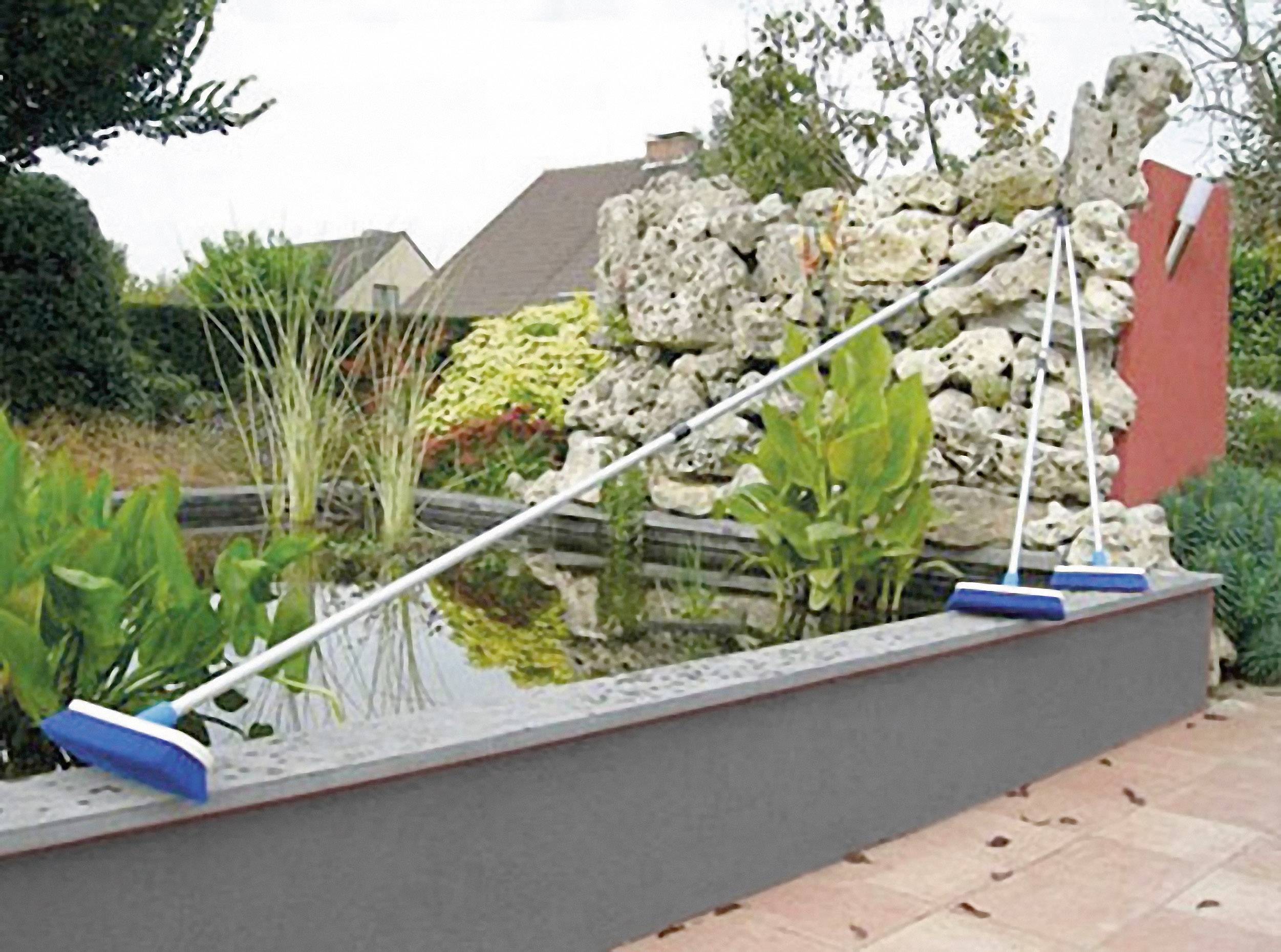 'Abdeckung für Teichrand', eine weiße Stange mit blauen Enden liegt quer über einem kleinen Gartenteich mit Pflanzen und Steinen im Hintergrund.