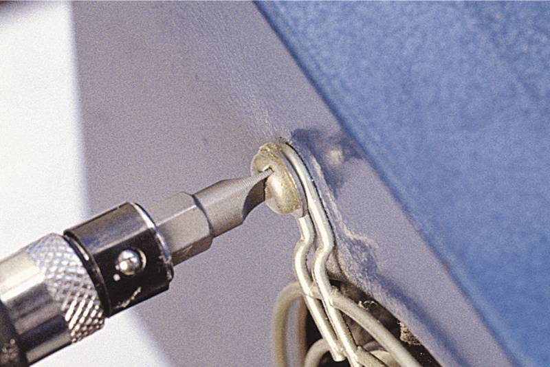 Ein Schraubendreher zieht eine Schraube in ein blaues Metallgehäuse. Drähte sind sichtbar.