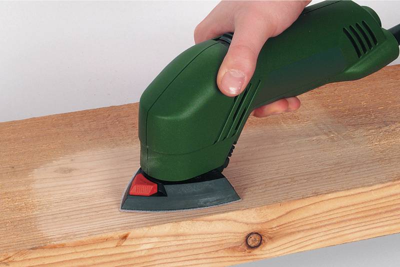 Eine Hand hält ein grünes Schleifgerät, das über ein Holzbrett gleitet, um die Oberfläche zu glätten.