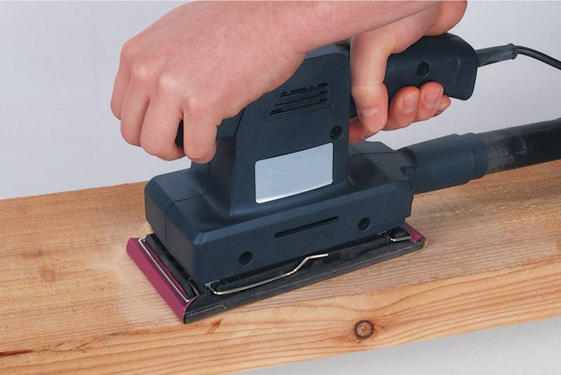 Eine Person schleift mit einem elektrischen Schleifgerät ein Holzbrett.