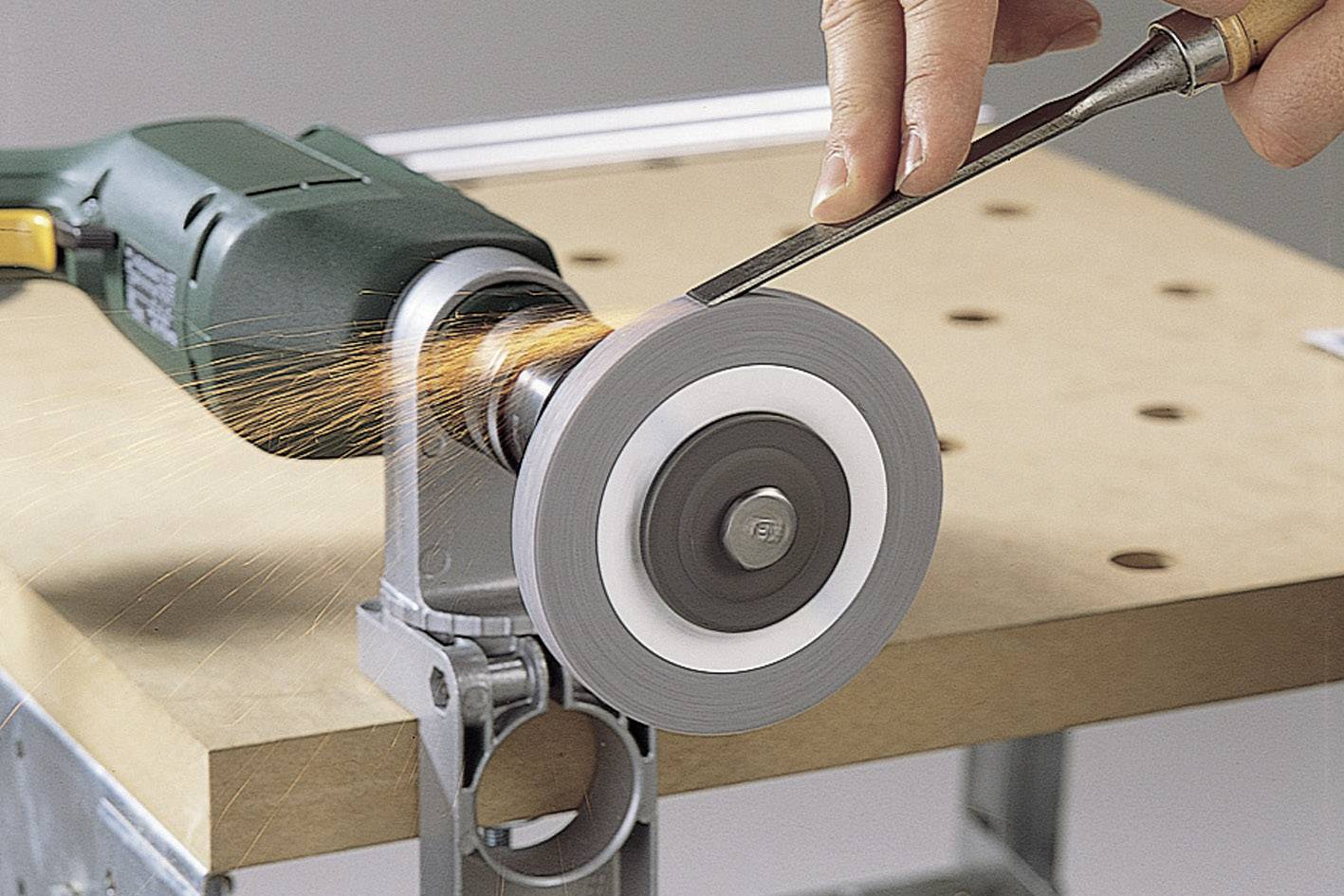 Eine Person schärft ein Metallwerkzeug mit einem elektrischen Schleifgerät auf einer Werkbank. Funken fliegen während des Prozesses.