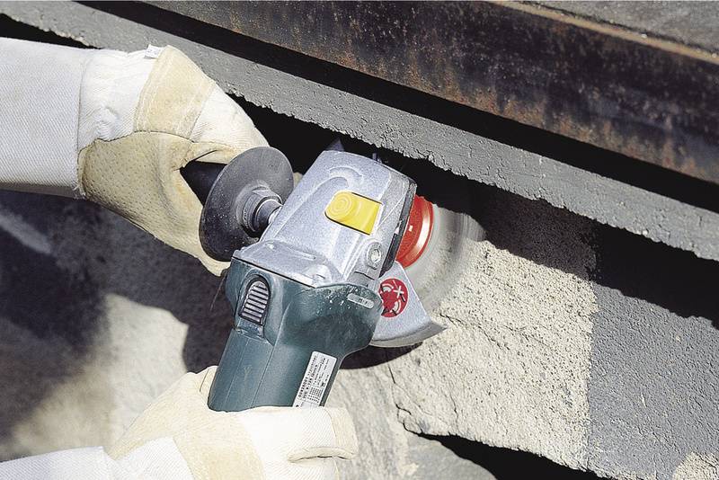 Handwerker schleift Beton mit Winkelschleifer, trägt Schutzhandschuhe.