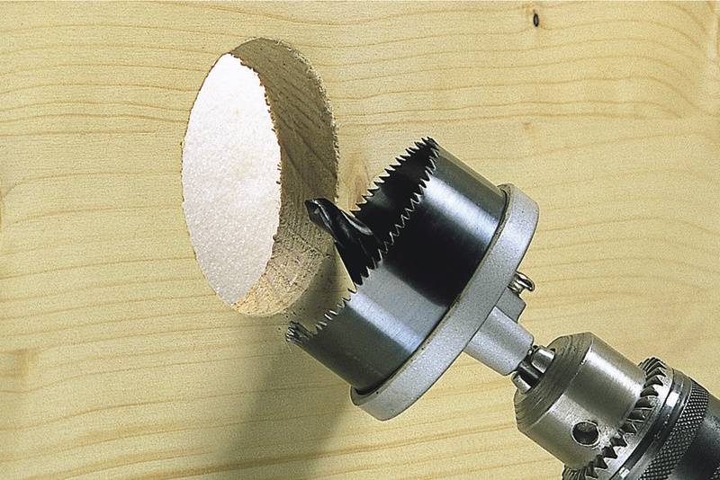 Ein Metallbohrer bohrt ein rundes Loch in ein Holzbrett. Der Bohrer hat scharfe Zähne und dreht sich, um das Holz effizient zu durchdringen.